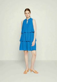 Vestido azul em camadas com decote halter e padrão texturizado. Combinado com sandálias laranjas de tiras.