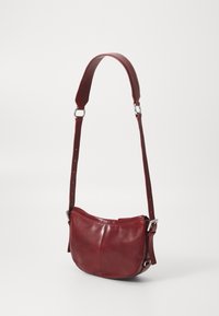 Borsa a spalla in pelle rossa con forma curvata, tracolla regolabile e dettagli in metallo argentato. Texture liscia con cuciture minime.