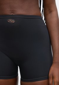 Čierne atletické šortky s hladkou textúrou, s logom na páse, navrhnuté pre pohodlie a pohyblivosť.