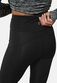 Svarta högmidjade leggings med en slät yta, sömmar och en liten reflektande detalj på bakre midjebandet.