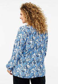 Langärmliges Hemd im blauen und weißen Blumenmuster, aus leichtem Stoff gefertigt. Hat einen lockeren Schnitt und einen runden Halsausschnitt, mit abgerundetem Saum.