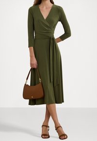 Olivgrön omslagsklänning med trekvartsärmar och en sidoknytdetalj. Brun handväska med rundad form och en kort axelrem. Bruna sandaletter med remmar.