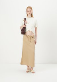 Puuvillane crop top lillemustriga, beež drawstring maxi seelik ja beež kõrgete kontsade sandaalid, koos pruuni käekotiga.