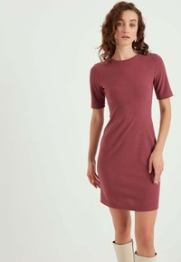 Ribbet bordeaux kjole med korte ærmer og en tætsiddende silhuet, der når til midten af låret, kombineret med knæhøje lyse beige støvler.