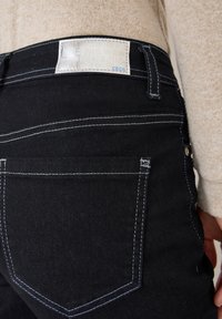 Jeans neri con cuciture bianche, dotati di un'etichetta patch sulla vita posteriore e tasche sul retro. Il materiale sembra denim.