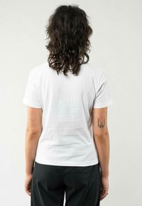 T-shirt en coton blanc vue de dos, avec un col rond, des manches courtes et une texture lisse. Design minimaliste sans motifs visibles.