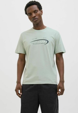 Hellgrünes Baumwoll-T-Shirt mit kurzen Ärmeln, das auf der Vorderseite ein schwarzes Grafik-Logo "CORE" zeigt; lässiger Schnitt und Rundhalsausschnitt.