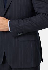 Jūras spēku pinstripe uzvalka žakete ar vienu krūšu kabatu, pogājamām piedurknēm, gludu auduma tekstūru un pielāgotu piegriezumu.