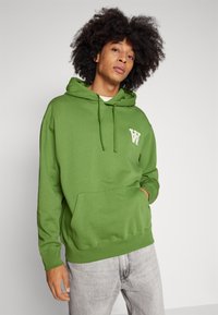 Green hoodie with a kangaroo pocket, drawstring hood, and white logo on the chest. Material appears soft; long sleeves with ribbed cuffs.