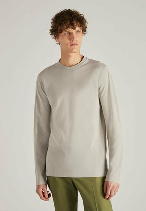 Lichtgrijze shirt met lange mouwen en een ronde hals, gemaakt van zacht materiaal, gecombineerd met groene broeken. Eenvoudig en aansluitend ontwerp met minimale details.