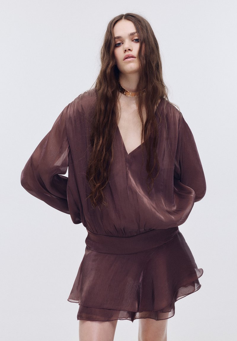 Rjava prosojna bluza z velikimi dolgimi rokavi in širokim pasom, združena s kratko večplastno krilo. Gladek tekstura, zasnova z V-izrezom.