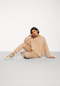 Sweatshirt oversized bege e calças de jogging combinando em tecido suave, com um pequeno detalhe de logotipo. Usado com tênis de cor clara.