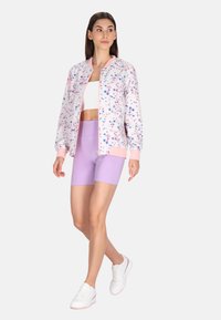 Lichtgewicht bomberjack in het wit met roze accenten en bloemenprint, gecombineerd met lila fietsshorts en witte sneakers.