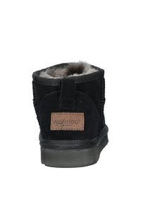 Zwarte suède enkellaars met een ronde neus, grijze bontvoering en een trekband aan de achterkant. Bevat een bruin leren logo patch op de hak.