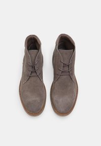 Botas de tobillo de ante marrón con una textura suave, punta redonda y diseño tradicional de cordones. Incluye dos ojales y una suela en contraste.