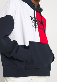 Felpa con cappuccio a blocchi di colore con pannelli blu navy, bianco e rosso. Presenta una tasca frontale a marsupio e un logo ricamato sul petto.