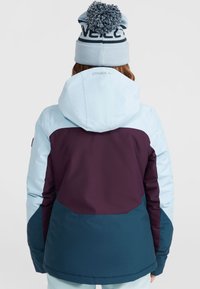 Veste à capuche isolée avec un design coloré comportant des sections bleu clair, violet foncé et turquoise. Texture douce, coupe décontractée.