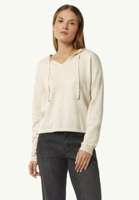 Cremfarbener, kurzer Hoodie mit V-Ausschnitt, Kordelzug und gerippten Bündchen. Weiche Textur mit lockerer Passform, kombiniert mit dunklen Jeans.