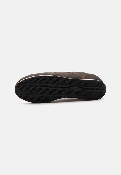 Semelle d'une chaussure marron avec une semelle en caoutchouc noire présentant un motif en chevrons et le nom de la marque embossé au centre.