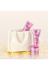 Vit fluffig väska med två rosa tuber och en rosa burk märkt "NUXE Hair Prodigieux." Produkterna är schampo, balsam och balsam.