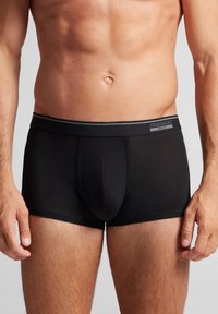 Svarta boxerkalsonger i slät tyg, med en grå midja med logotyp. Designen inkluderar sömnadsdetaljer och en stödjande frontficka.