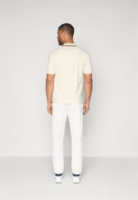 Kratka polo majica kremaste barve s kontrastnim ovratnikom in slim fit krojem, v kombinaciji z belimi hlačami in belimi tenisicami.