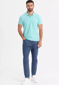 Ljusblå polo t-shirt med krage, tillsammans med blå denimjeans och vita sneakers. T-shirten har en liten logotyp på bröstet.