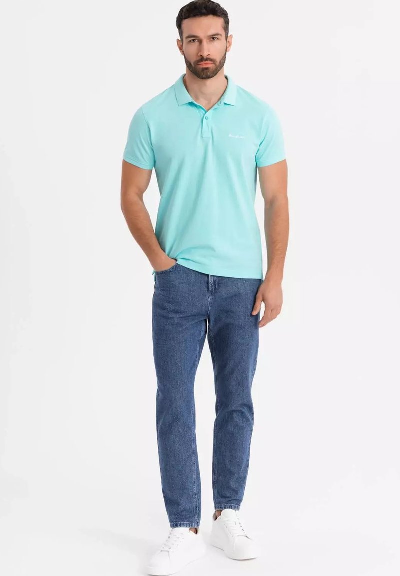 Ljusblå polo t-shirt med krage, tillsammans med blå denimjeans och vita sneakers. T-shirten har en liten logotyp på bröstet.