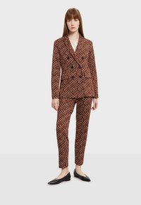 Ruskean kuviollinen jakku ja housut, joissa on kaksoisnapitus, mustat napit ja slim fit -malli. Yhdistetty mustien matalakorkoisten kenkien kanssa.