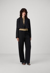 Musthave, musthave, beige top, kõrge vöökohaga mustad püksid ja mustad avatud varvastega sandaalid; sile kangas, selged jooned ja kohandatud istuvus.