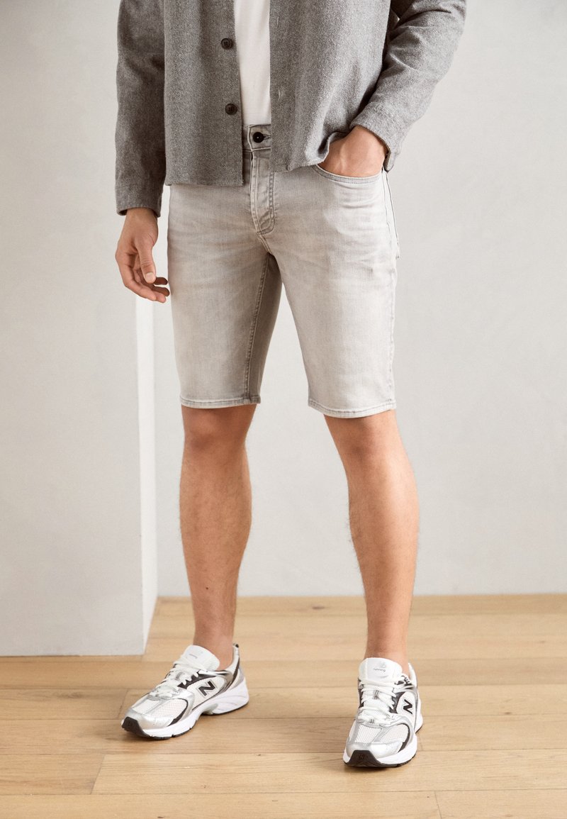Light gray denim shorts with a slim fit and frayed hem, paired with a white shirt, gray cardigan, and silver athletic shoes.