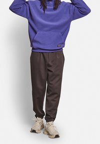 Violetti huppari etutaskulla, yhdistetty tummanruskeisiin kapealahkeisiin housuihin ja vaaleisiin lenkkareihin. Mukava, rento urheilullinen asu.