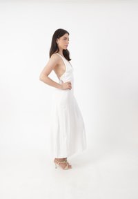 Abito lungo bianco senza maniche con scollatura a V profonda e design con schiena scoperta, realizzato in tessuto morbido con una silhouette fluida.