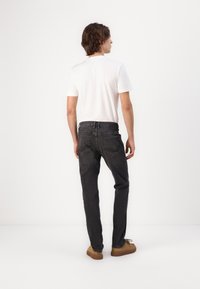 Jeans en denim noir avec une coupe slim, dotés de poches arrière, d'une fermeture à bouton en métal et de détails cousus, présentés avec un t-shirt blanc.