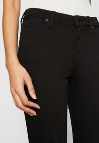 Jeans in denim nero con una vestibilità slim, dotati di tasche frontali, una superficie liscia e dettagli di cucitura discreti lungo le cuciture.