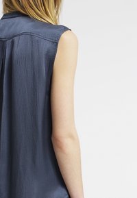 Ärmelloses navy-blaues Top mit strukturiertem Finish, das über eine dezente Faltendetail am Rücken verfügt und eine lässige Passform sowie einen weichen Stoff hervorhebt.