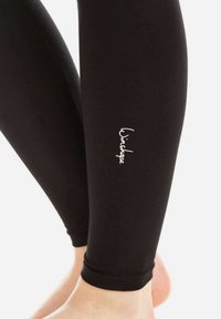 Svarta leggings i elastiskt tyg, med en tajt passform och en vit logotyp på underbenet. Benslutet är rundat vid ankeln.