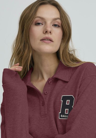 Bordó, hosszú ujjú pólóing, gallérral, két gombbal, és hímzett "B" logóval a bal mellrészen. Puha, enyhén texturált anyag.