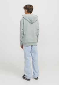 Felpa verde chiaro realizzata in tessuto morbido, con tasca a marsupio e vestibilità oversize. Abbinata a jeans in denim blu chiaro.