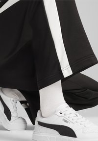 Mustad mustad sportsijalatsid valge külgtriibuga, koos valgete tennisekatega, millel on must Puma logo. Sile kangas ja juhuslik disain.