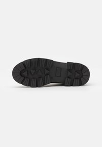 Suela de zapatilla negra de goma con surcos profundos y patrones angulares. Presenta un área de acolchado rectangular para soporte. Diseño ligero y texturizado.