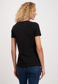 Czarna koszulka z krótkim rękawem o okrągłym dekolcie, miękka w dotyku, dopasowany krój i gładki tył, w zestawie z niebieskimi dżinsami.