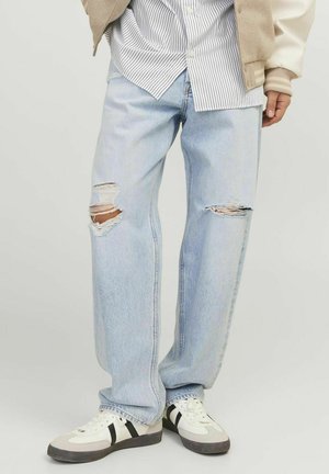 Lyseblå slidte jeans med store huller ved knæene, parret med en stribet skjorte og hvide sneakers med sorte accenter.