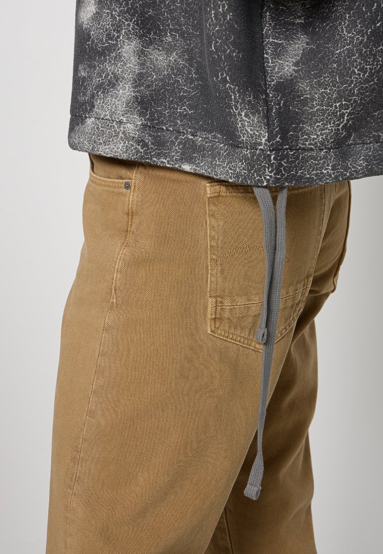 Grauer, strukturierter Sweatshirt mit einem Spritzmuster, kombiniert mit tanfarbenen, Canvas-Hosen, die über eine Gesäßtasche und einen grauen Kordelzug verfügen.