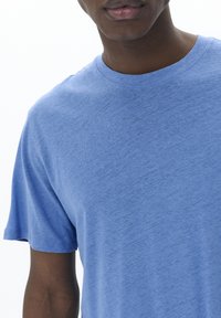 Blå t-shirt med kortärmar, tillverkad av mjukt material, med rundad halsringning och en lätt texturerad yta, i en avslappnad passform.