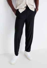 Black, ribbed jogger pants with an elastic waistband and drawstring, paired with white sneakers. The fabric appears lightweight and casual.