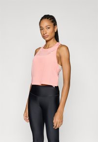 Top atlético rosa recortado com textura em malha, decote redondo e design racerback, combinado com leggings pretas de cintura alta.