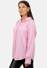 Camicia rosa con texture e motivi di cuori bianchi, con bottoni frontali, vestibilità rilassata e maniche lunghe.