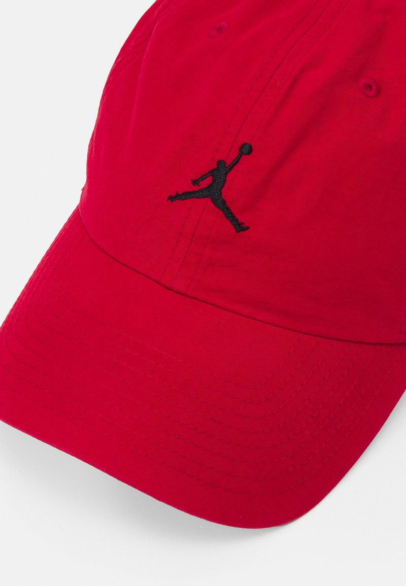 Casquette rouge en tissu de coton, arborant un logo Jumpman brodé en noir. Le design comprend des accents cousus sur la visière et la couronne.