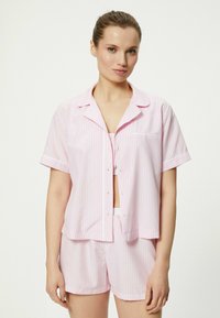 Conjunto de pijama de manga corta a rayas de color rosa claro, con una camiseta abotonada y pantalones cortos a juego, confeccionado en una tela suave y con un corte relajado.